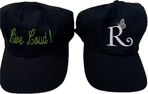 The two Rebellious Aging hats side by side: a black cap with “Live Loud!” in green script, and a black cap with the white R and butterfly logo.